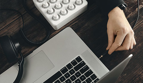 hand using laptop with headphones and audio controller for 8 track production