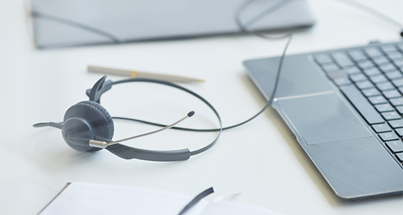 headset resting next to a laptop on a desk with a pen and notepad tools for three way communication