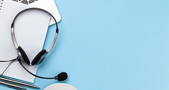 a headset rests on a blue desk next to a laptop a notepad and two pens providing a workspace for communication and productivity